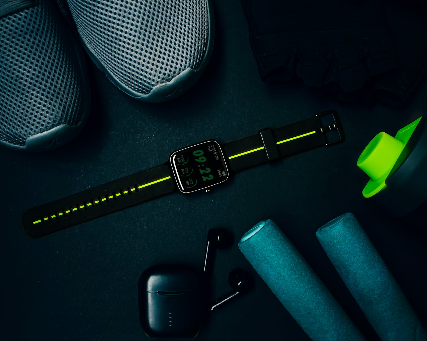 Fitness accessories arranged on a dark surface including a smartwatch, shoes, and rollers.