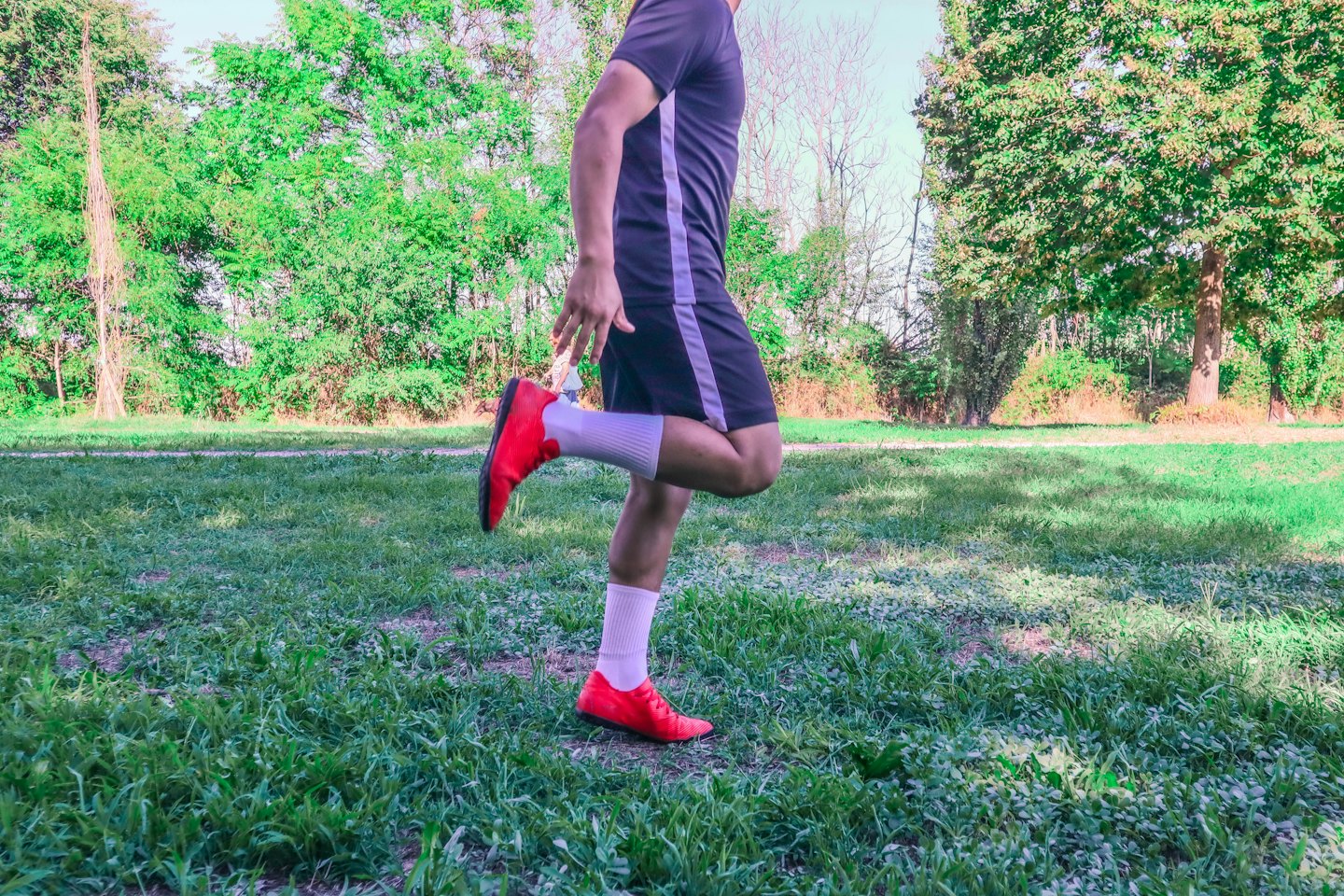 Person stretching leg in a park with green trees.