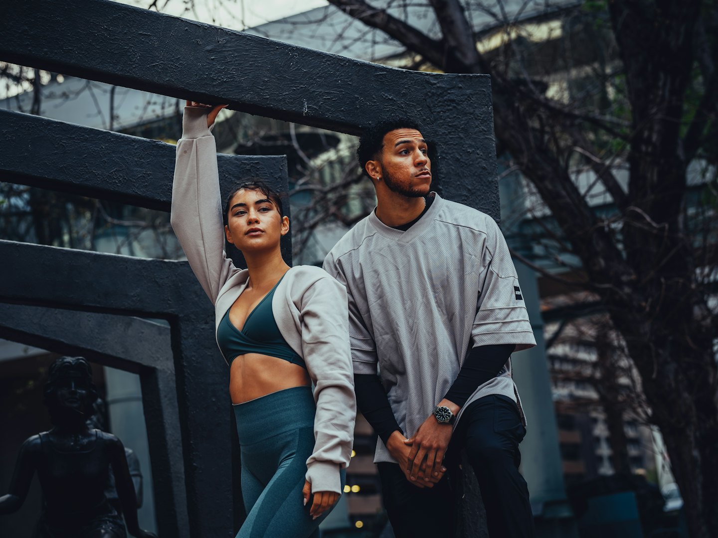 Fitness models pose in activewear near concrete structures and bare trees.